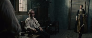 Movie still from “Tulip Fever” (2017), directed by Justin Chadwick – A man sitting on a chair in a room; Medium shot, High angle
