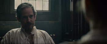 Movie still from “Tulip Fever” (2017), directed by Justin Chadwick – A man wearing a white shirt sitting in front of a window; Close Up shot, Over the shoulder angle
