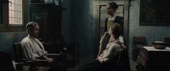 Movie still from “Tulip Fever” (2017), directed by Justin Chadwick – Two women sitting on a chair in front of a fireplace; Medium shot, High angle