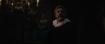 Movie still from “Tulip Fever” (2017), directed by Justin Chadwick – A man wearing a black and white collar and standing next to a candle; Medium shot, Over the shoulder angle
