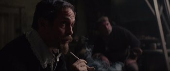 Movie still from “Tulip Fever” (2017), directed by Justin Chadwick – A man smoking a cigarette while another man watches; Medium shot, Over the shoulder angle