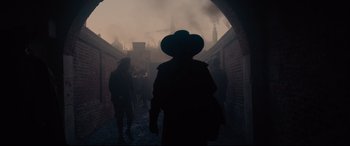 Movie still from “Tulip Fever” (2017), directed by Justin Chadwick – A man in a hat is walking through a tunnel; Wide shot, Over the shoulder angle