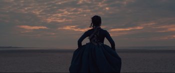 Movie still from “Tulip Fever” (2017), directed by Justin Chadwick – A woman standing on the beach at sunset; Wide shot, Low angle