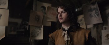 Movie still from “Tulip Fever” (2017), directed by Justin Chadwick – A man with long brown hair wearing a brown and white shirt; Medium shot, Over the shoulder angle