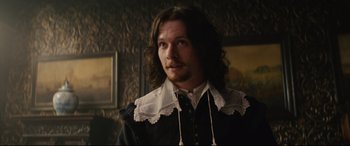 Movie still from “Tulip Fever” (2017), directed by Justin Chadwick – A man with long brown hair wearing a black and white shirt; Medium shot, Low angle