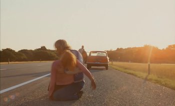 Movie still from “Turkish Delight” (1973), directed by Paul Verhoeven – A woman kneeling on the side of the road while a car is parked in front of it; Wide shot, Low angle