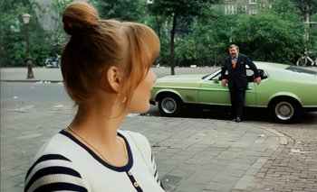 Movie still from “Turkish Delight” (1973), directed by Paul Verhoeven – A woman standing in front of a green car and a man in a suit; Wide shot, Over the shoulder angle