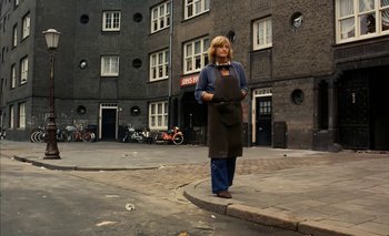 Movie still from “Turkish Delight” (1973), directed by Paul Verhoeven – A woman standing on a street corner wearing an apron; Wide shot, High angle