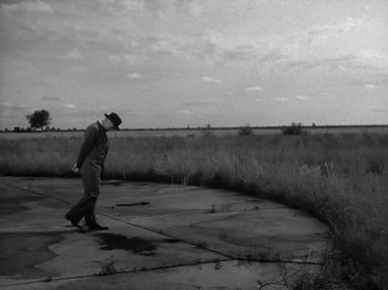 Movie still from “Twelve O'Clock High” (1949), directed by Henry King – A man walking across a concrete slab near a field; Extreme Wide shot, High angle
