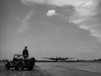Movie still from “Twelve O'Clock High” (1949), directed by Henry King – An airplane is flying in the sky near a jeep; Extreme Wide shot, Low angle