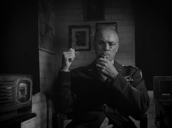 Movie still from “Twelve O'Clock High” (1949), directed by Henry King – A man in uniform smoking a cigarette in a room; Medium shot, Low angle