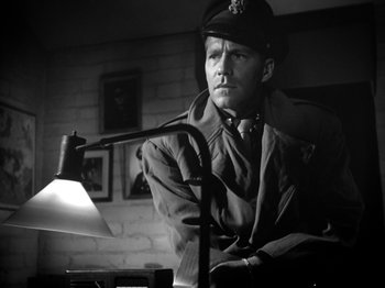Movie still from “Twelve O'Clock High” (1949), directed by Henry King – A man wearing a uniform and a hat is sitting in front of a lamp; Close Up shot, Low angle
