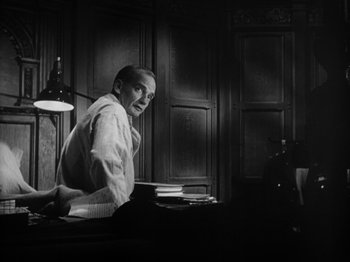 Movie still from “Twelve O'Clock High” (1949), directed by Henry King – A man sitting at a desk in front of a lamp; Medium shot, Low angle