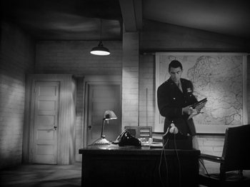 Movie still from “Twelve O'Clock High” (1949), directed by Henry King – A man standing at a desk in a room; Wide shot, High angle