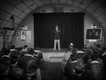 Movie still from “Twelve O'Clock High” (1949), directed by Henry King – An air force officer stands in front of an audience; Wide shot, Low angle