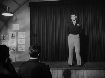 Movie still from “Twelve O'Clock High” (1949), directed by Henry King – A man standing on a stage in front of another man; Wide shot, Low angle
