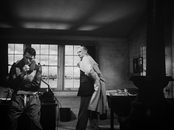 Movie still from “Twelve O'Clock High” (1949), directed by Henry King – A man in a suit and tie standing in front of a table; Medium shot, Low angle