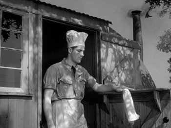 Movie still from “Twelve O'Clock High” (1949), directed by Henry King – A man wearing a chef's hat standing in front of a building; Medium shot, Low angle