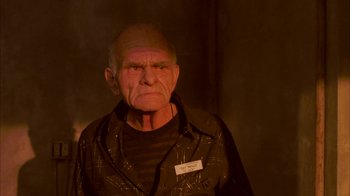 Movie still from “Twin Peaks: Fire Walk with Me” (1992), directed by David Lynch – An old man wearing a black shirt and a name tag; Close Up shot, Low angle