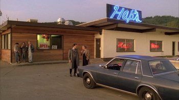 Movie still from “Twin Peaks: Fire Walk with Me” (1992), directed by David Lynch – Two men standing outside of a restaurant next to a parked car; Wide shot, Low angle