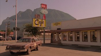 Movie still from “Twin Peaks: Fire Walk with Me” (1992), directed by David Lynch – A car parked in front of a cafe with mountains in the background; Extreme Wide shot, Low angle
