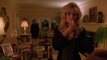 Movie still from “Twin Peaks: Fire Walk with Me” (1992), directed by David Lynch – A woman smoking a cigarette in a living room; Medium shot, Low angle
