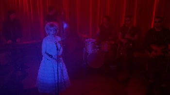 Movie still from “Twin Peaks: Fire Walk with Me” (1992), directed by David Lynch – A woman singing into a microphone in front of a band; Wide shot, High angle