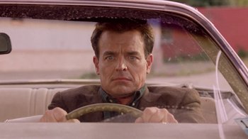 Movie still from “Twin Peaks: Fire Walk with Me” (1992), directed by David Lynch – A man driving a car in the back of a car; Close Up shot, Over the shoulder angle