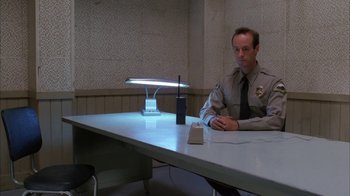 Movie still from “Twin Peaks: Fire Walk with Me” (1992), directed by David Lynch – A man sitting at a table in a jail cell; Medium shot, High angle