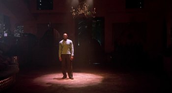 Movie still from “Two Can Play That Game” (2001), directed by Mark Brown – A man standing in a dimly - lit room in front of a chandelier; Wide shot, Low angle