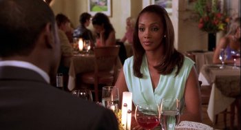 Movie still from “Two Can Play That Game” (2001), directed by Mark Brown – A woman sitting at a table with a glass of wine in front of her; Medium shot, Over the shoulder angle