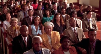 Movie still from “Two Can Play That Game” (2001), directed by Mark Brown – A large group of people sitting in a room together; Wide shot, High angle