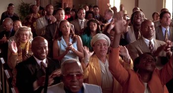 Movie still from “Two Can Play That Game” (2001), directed by Mark Brown – A group of people sitting in a room with their hands raised; Medium shot, High angle