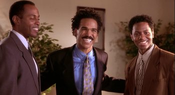 Movie still from “Two Can Play That Game” (2001), directed by Mark Brown – A man in a suit and tie smiling for the camera; Medium shot, Low angle