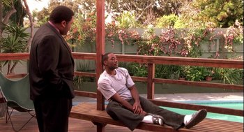 Movie still from “Two Can Play That Game” (2001), directed by Mark Brown – A man sitting on top of a wooden bench next to another man; Wide shot, High angle