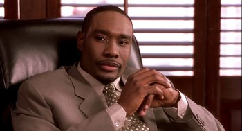 Movie still from “Two Can Play That Game” (2001), directed by Mark Brown – A man sitting in a chair wearing a suit and tie; Close Up shot, Low angle