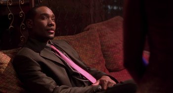 Movie still from “Two Can Play That Game” (2001), directed by Mark Brown – A man sitting on a couch wearing a suit and tie; Close Up shot, High angle