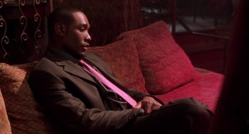 Movie still from “Two Can Play That Game” (2001), directed by Mark Brown – A man sitting on a couch wearing a suit and pink tie; Medium shot, High angle