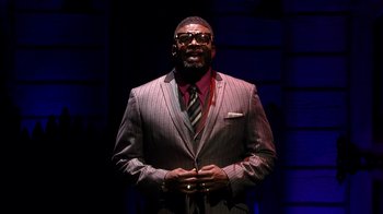 Movie still from “Madea on the Run” (2017), directed by Derrick Doose – A man wearing a suit and tie standing in front of a building; Medium shot, Low angle