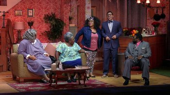 Movie still from “Madea on the Run” (2017), directed by Derrick Doose – A group of people standing around a living room; Wide shot, High angle