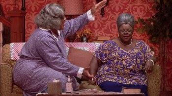 Movie still from “Madea on the Run” (2017), directed by Derrick Doose – Two women sitting on a couch and one of the women is holding her hand up to the other; Medium shot, High angle