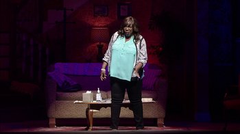 Movie still from “Madea on the Run” (2017), directed by Derrick Doose – A woman standing on a stage in front of a living room; Wide shot, High angle