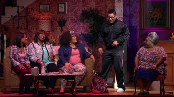 Movie still from “Madea on the Run” (2017), directed by Derrick Doose – A group of people sitting on top of a couch on a stage; Wide shot, Over the shoulder angle
