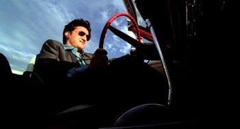 Movie still from “U Turn” (1997), directed by Oliver Stone – A man in a suit and sunglasses driving a car; Medium shot, Low angle
