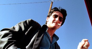 Movie still from “U Turn” (1997), directed by Oliver Stone – A man wearing sunglasses and holding a cigarette; Close Up shot, Low angle