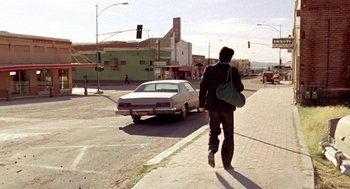 Movie still from “U Turn” (1997), directed by Oliver Stone – A man walking down a street past a parked car; Wide shot, Low angle