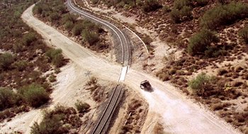 Movie still from “U Turn” (1997), directed by Oliver Stone – An aerial view of train tracks and a truck on the side of the road; Extreme Wide shot, Overhead angle