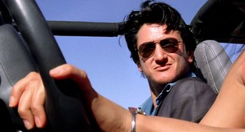 Movie still from “U Turn” (1997), directed by Oliver Stone – A person wearing sunglasses and holding a steering wheel; Close Up shot, Low angle