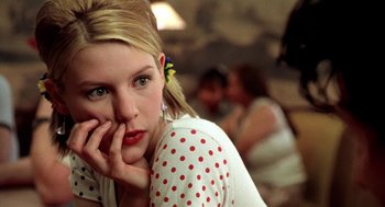 Movie still from “U Turn” (1997), directed by Oliver Stone – A woman with a red flower in her hair and polka dot shirt; Close Up shot, Low angle