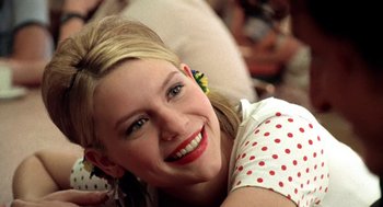 Movie still from “U Turn” (1997), directed by Oliver Stone – A woman smiling for the camera while sitting on the ground; Close Up shot, Over the shoulder angle